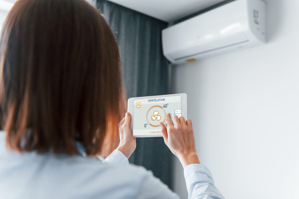 A person using a tablet to control the ventilation settings of an air conditioning unit. Understanding how to clean your air ducts can improve the efficiency of such smart HVAC systems.