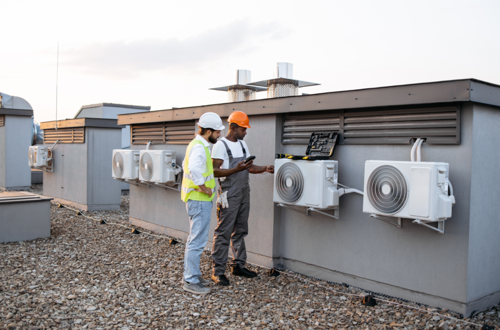 Two technicians inspect and maintain HVAC systems on a commercial rooftop, demonstrating the importance of regular maintenance in learning how to clean your air ducts effectively.