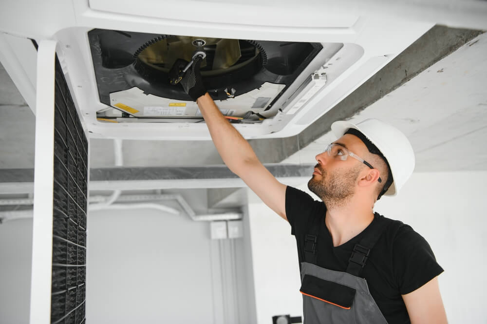 A technician cleaning an air conditioner system, ensuring improved air quality and efficiency. Because he knows the answer to the question - what does air duct cleaning do? 