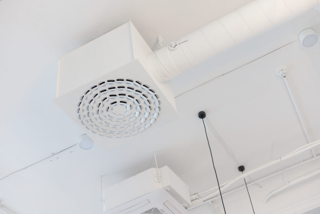 A white ceiling-mounted ventilation duct system with circular vents, designed to efficiently circulate air throughout the space.